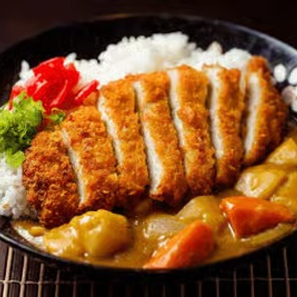 Japanese-style breaded chicken cutlet over rice with curry, potatoes, carrots, and red peppers in a black bowl.