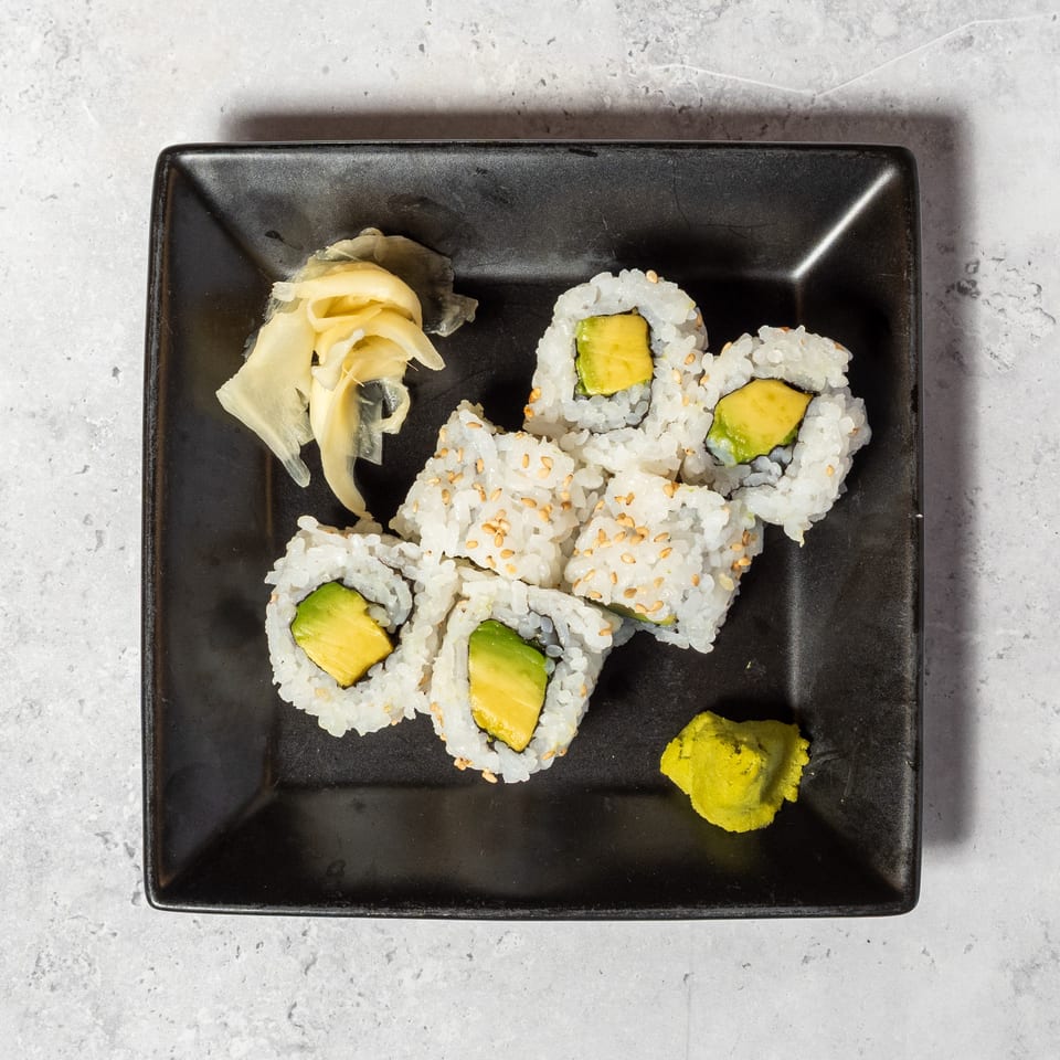 Sushi rolls filled with avocado and cucumber, sprinkled with sesame seeds, served on a black plate with pickled ginger and wasabi.