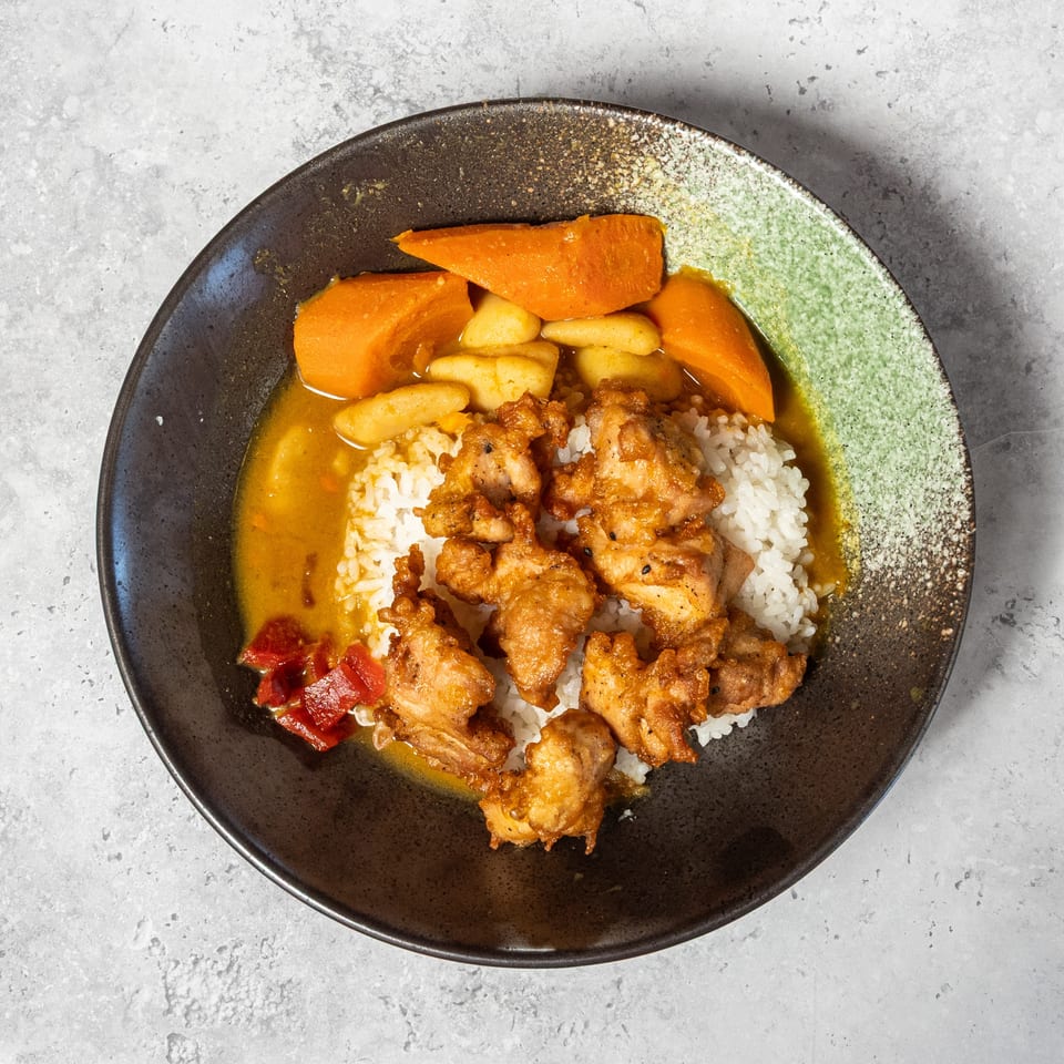 Bowl of white rice topped with crispy fried chicken, Japanese curry sauce, carrots, potatoes, and red peppers.