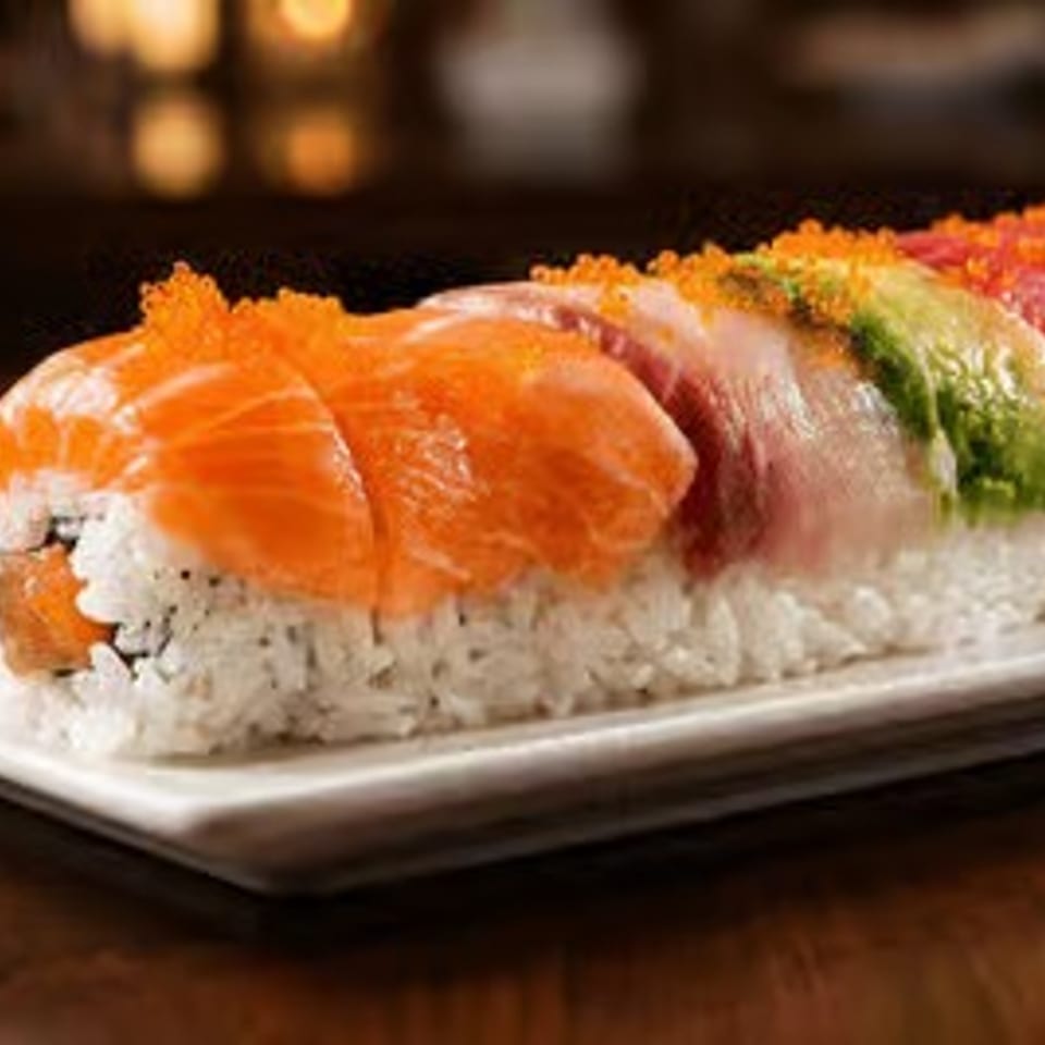 Colorful assorted sushi rolls topped with salmon, tuna, shrimp, and vegetables on a white rectangular plate.